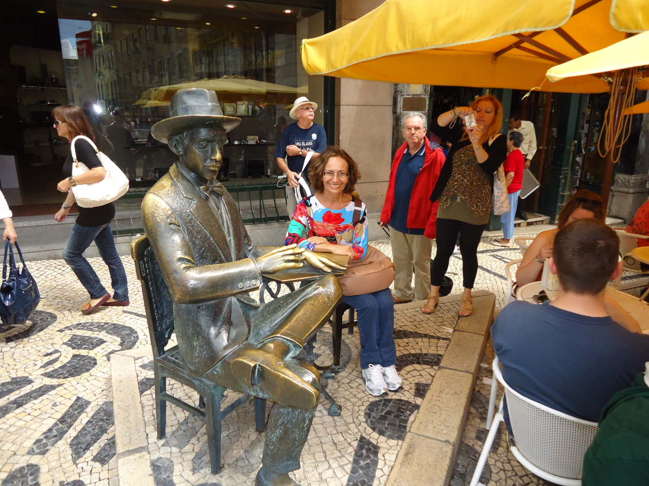 Eu sentado com a estátua de Fernando Pessoa em Lisboa.